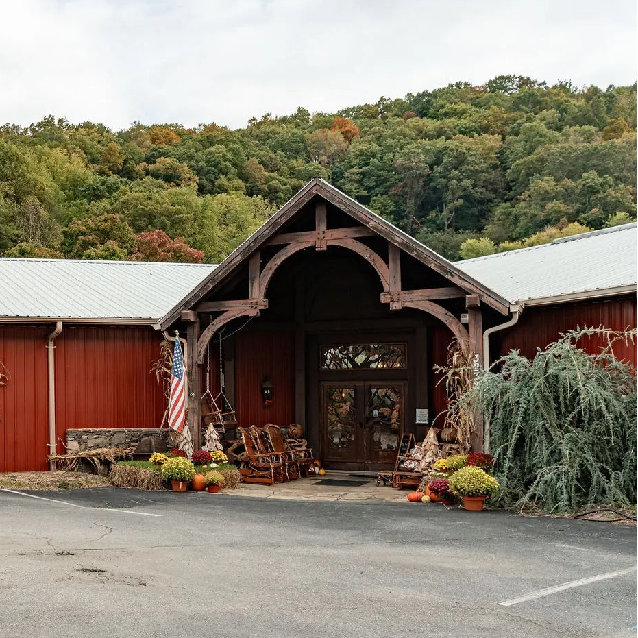 High Country Furniture Design store exterior with a red metal building, covered parking lot, and wooded hillside in the background.